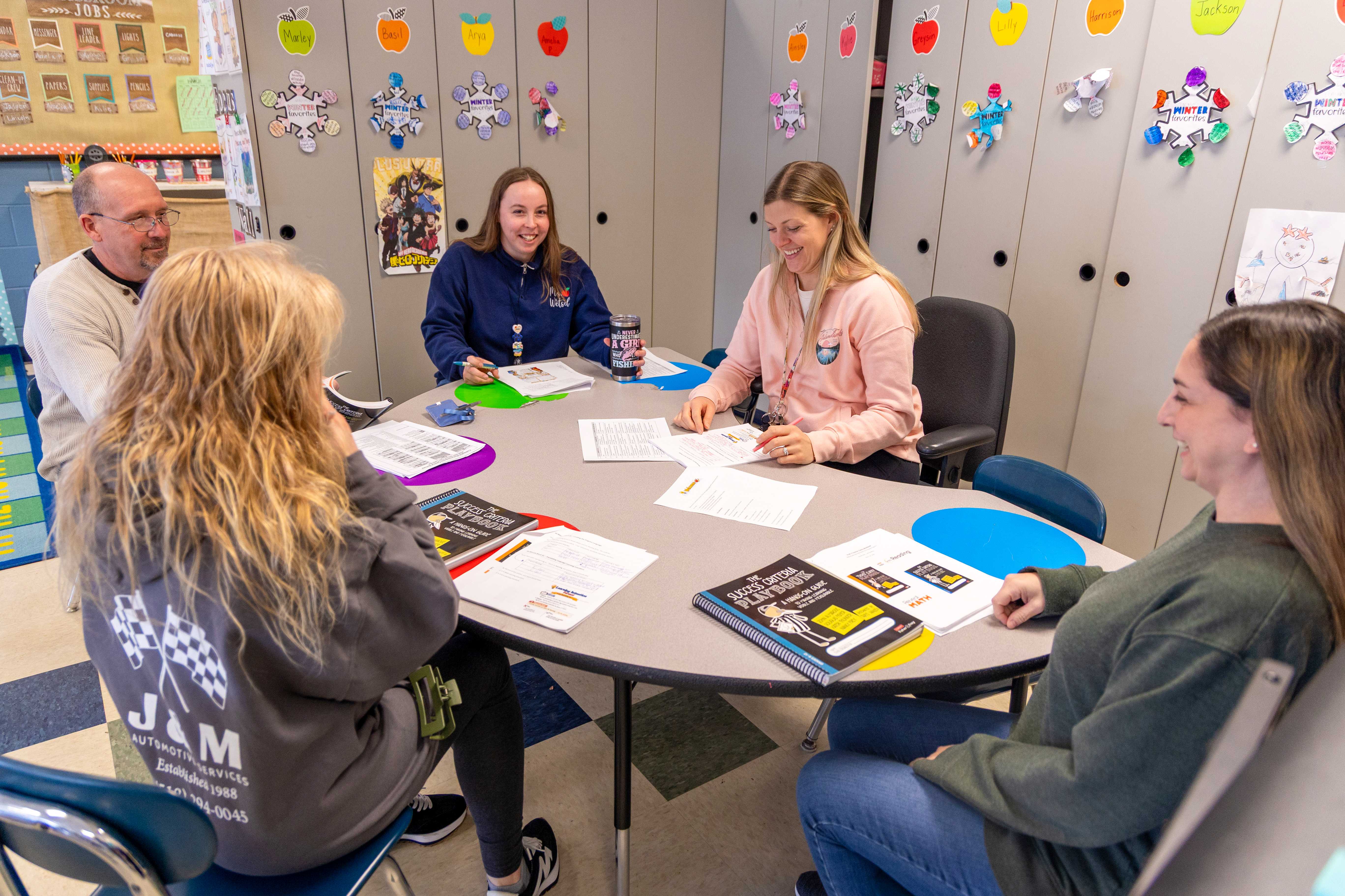 A group of elementary educators smiles while working in their booklets together